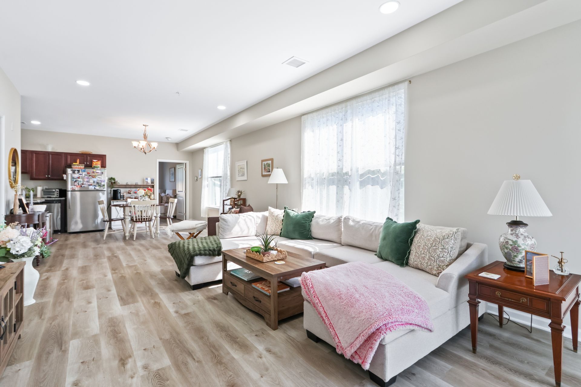 Spacious living room with sectional sofa, coffee table, and open kitchen. Light wood floors and neutral walls.