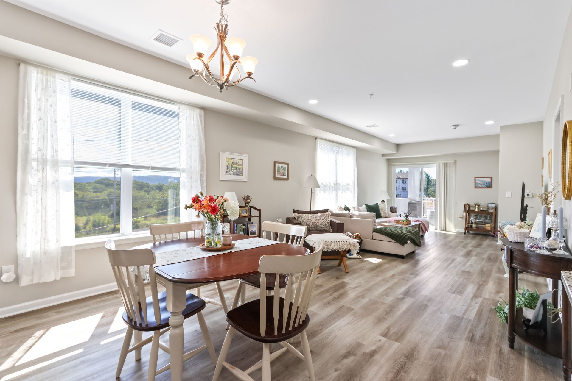 Spacious, open-concept living space with dining table, sofa, and access to a balcony; light wood floors, neutral tones.