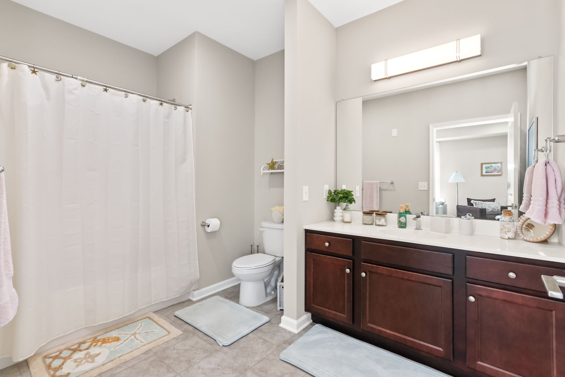 Bathroom with dark brown vanity, white countertop, large mirror, and shower with a white curtain.
