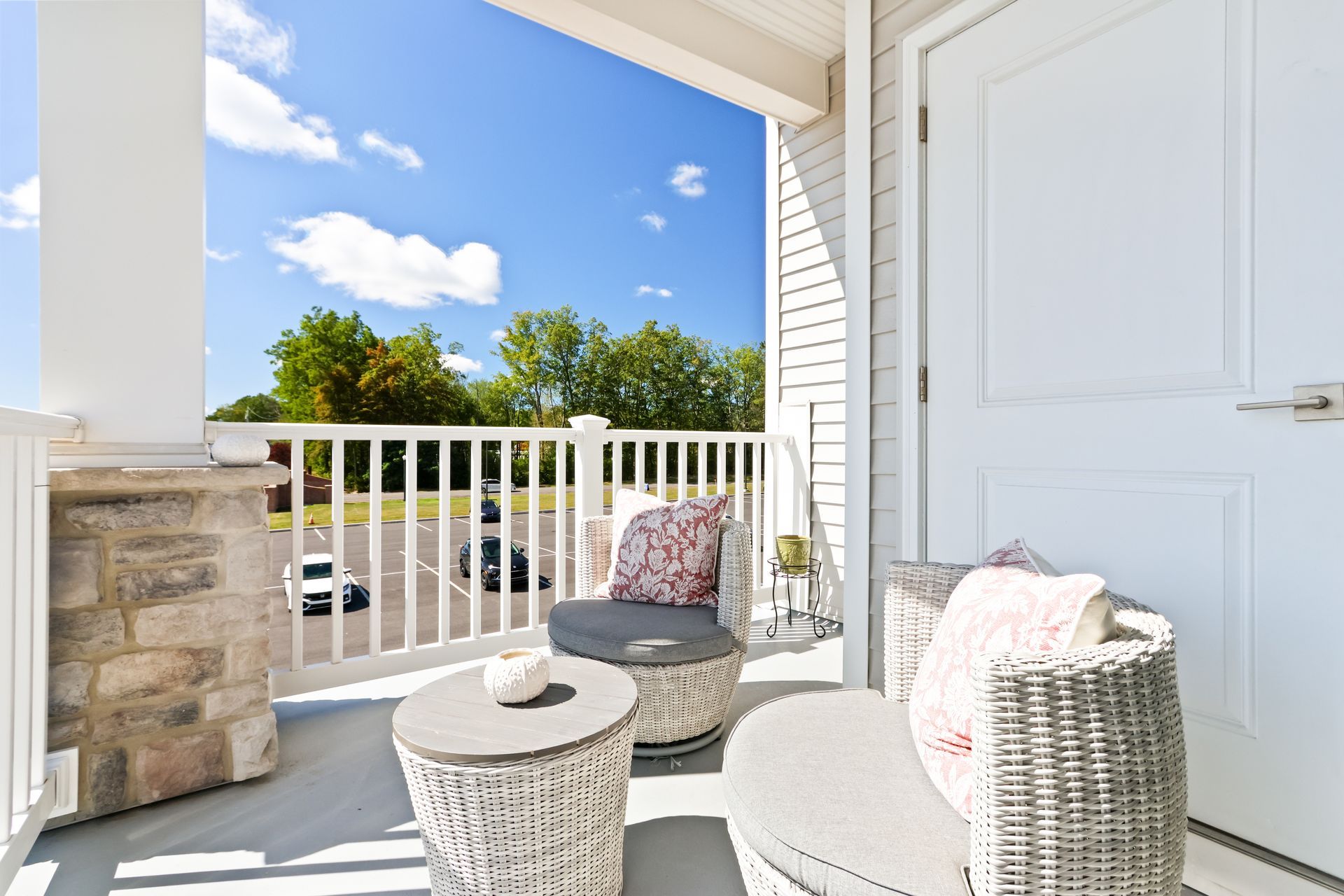 Balcony with white wicker furniture, blue sky, and a view of trees and cars.