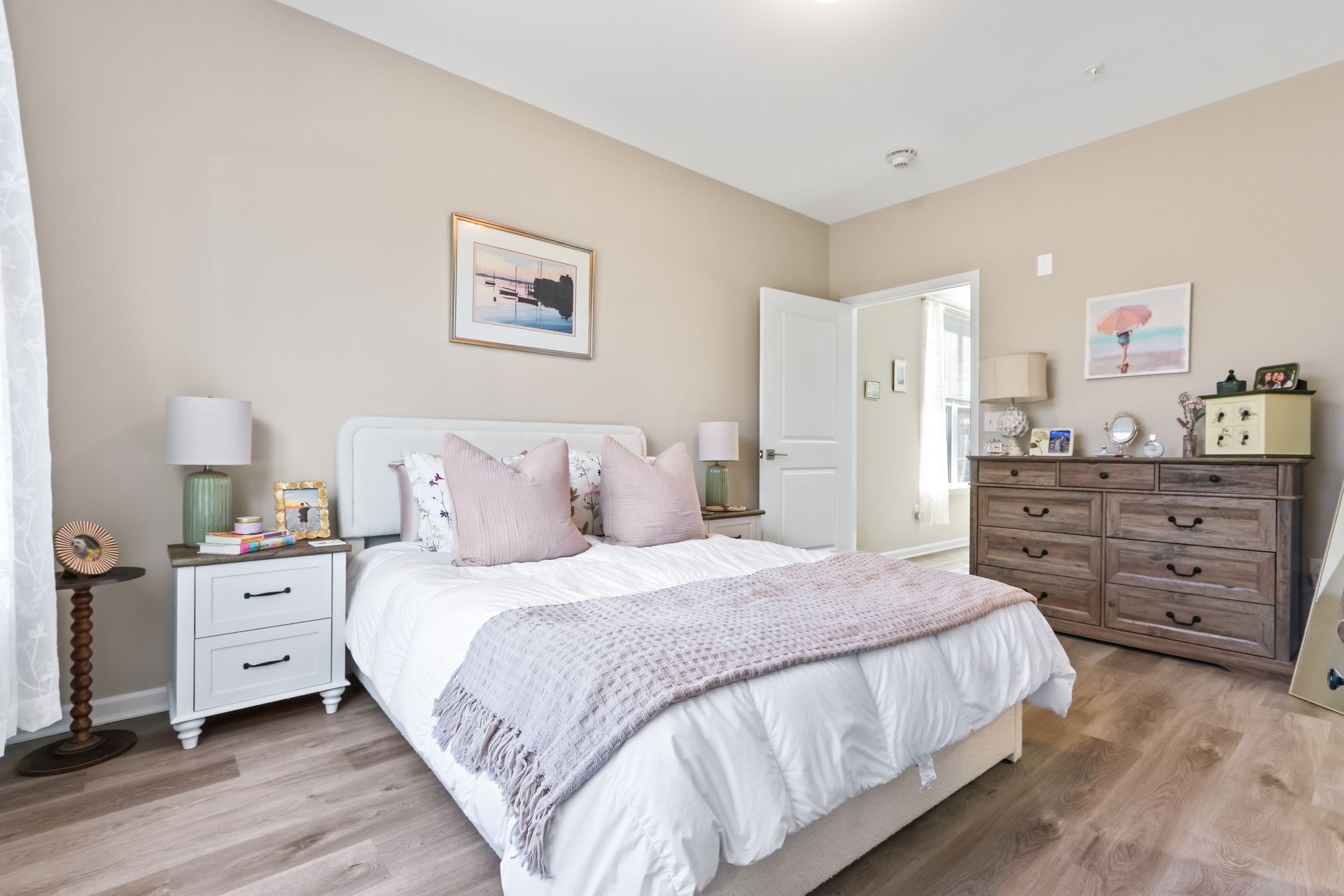 Bedroom with a white bed, pink pillows, light wood furniture, and artwork.