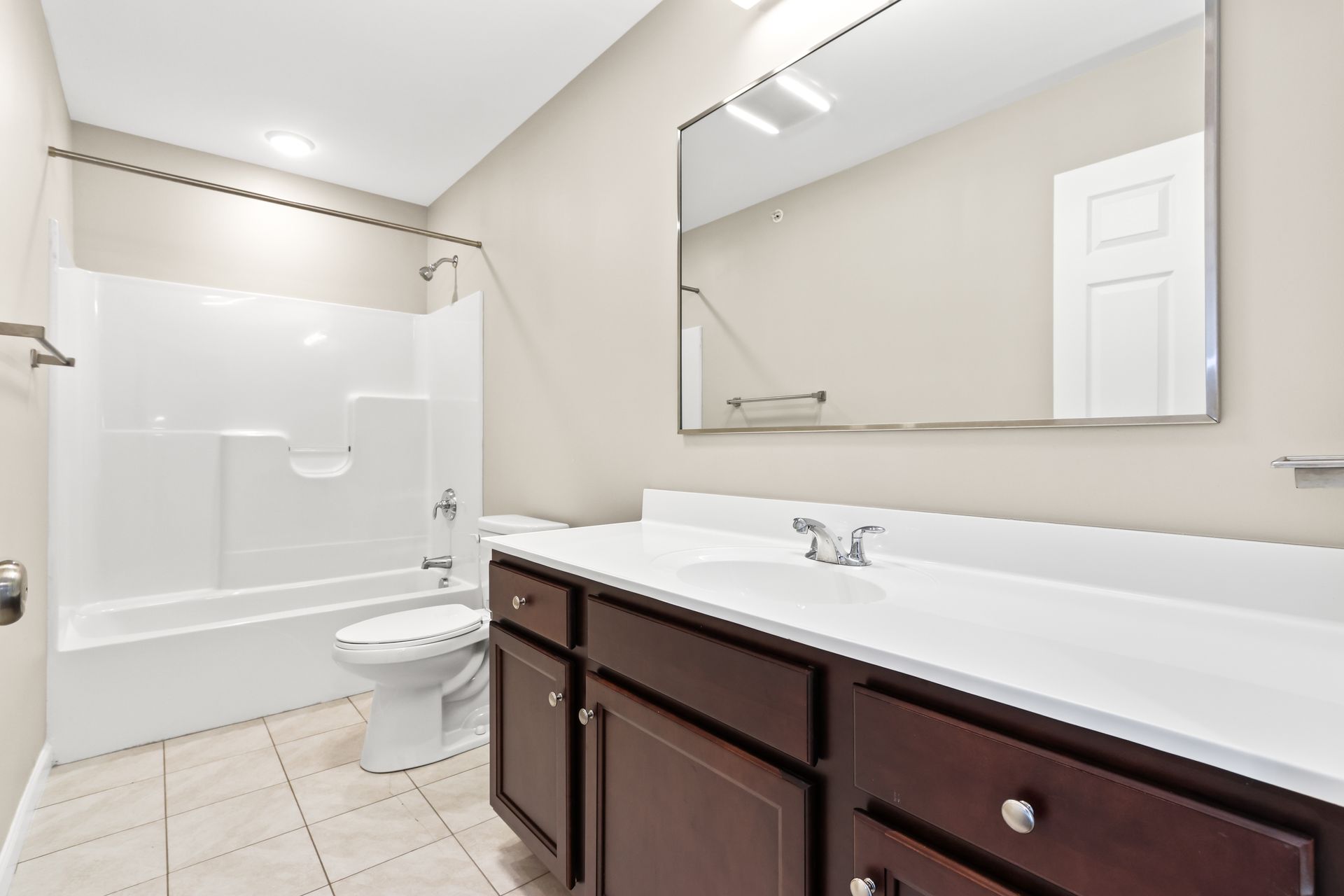 Bathroom with white tub, toilet, dark cabinets, and large mirror.