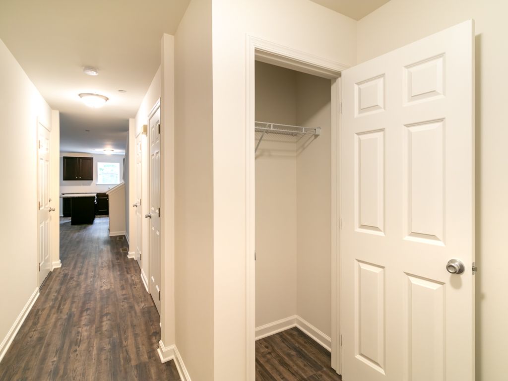 Hallway with wood-look flooring, white walls, and an open closet. The kitchen is visible at the end.