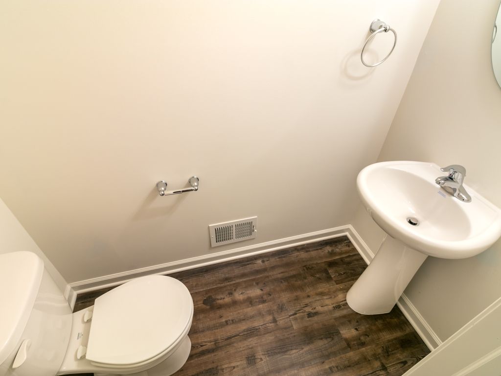 Small bathroom with toilet, pedestal sink, and silver fixtures on a wood-look floor.