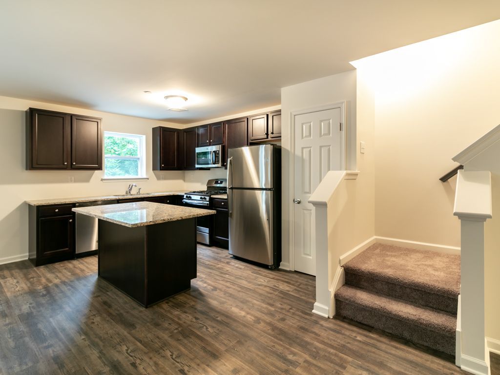 Kitchen with dark cabinets, stainless steel appliances, island, and stairs to the upper level.