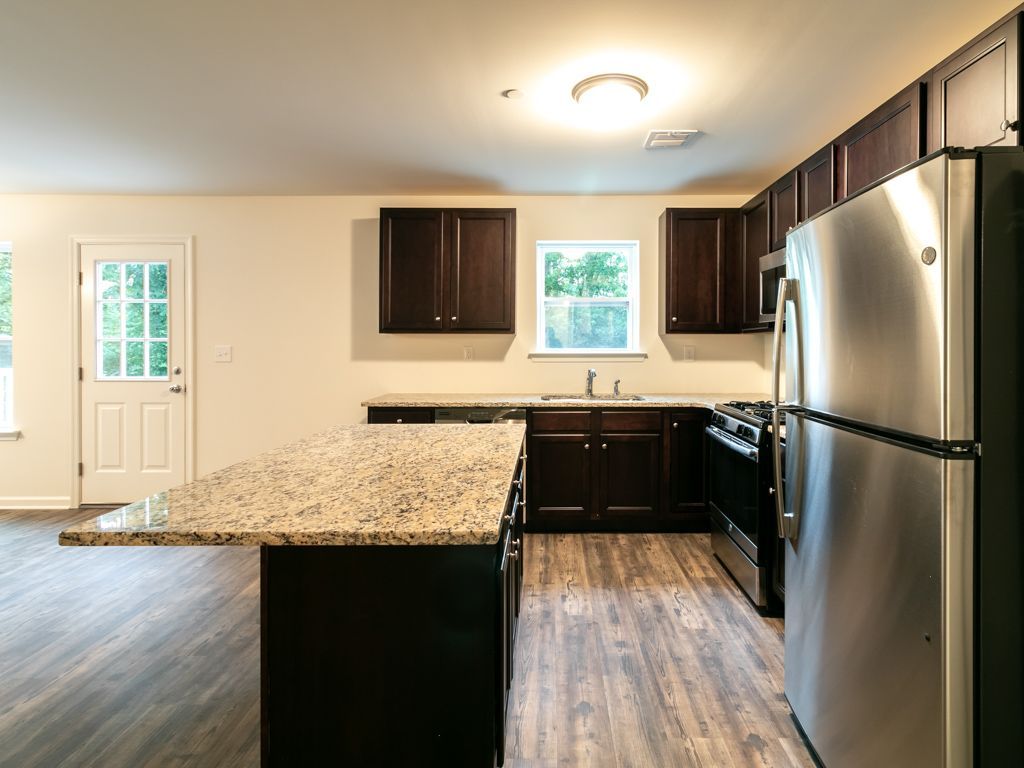 Kitchen with granite countertop island, dark wood cabinets, stainless steel appliances, and door to the outside.