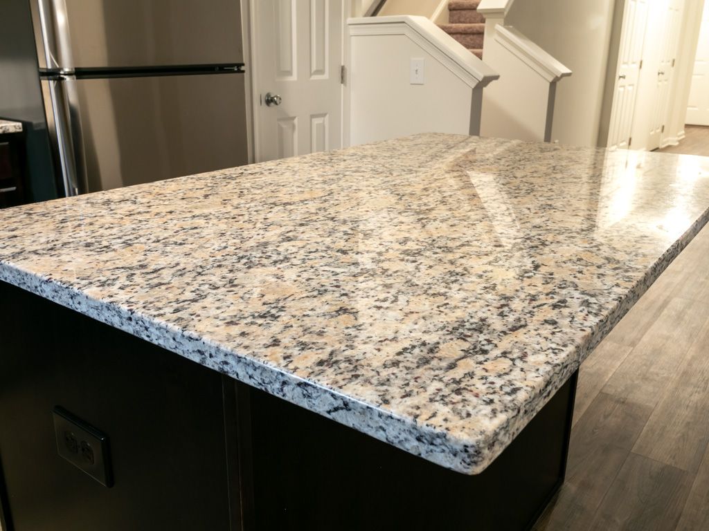 Kitchen island with granite countertop, dark cabinets, and stainless steel refrigerator.