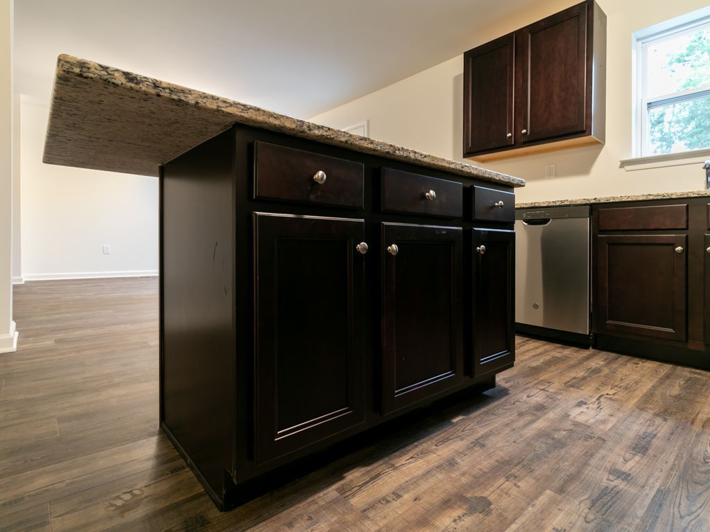 Kitchen island with dark cabinets, granite countertop, and wood flooring.