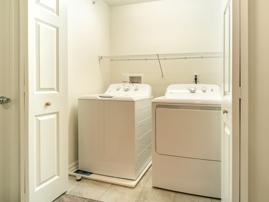 Laundry room with white washer and dryer, shelf above.