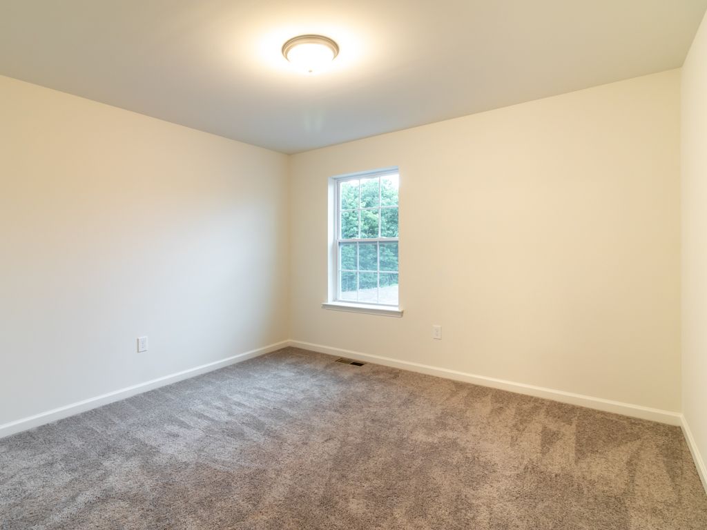 Empty room with beige walls, brown carpet, and a window.