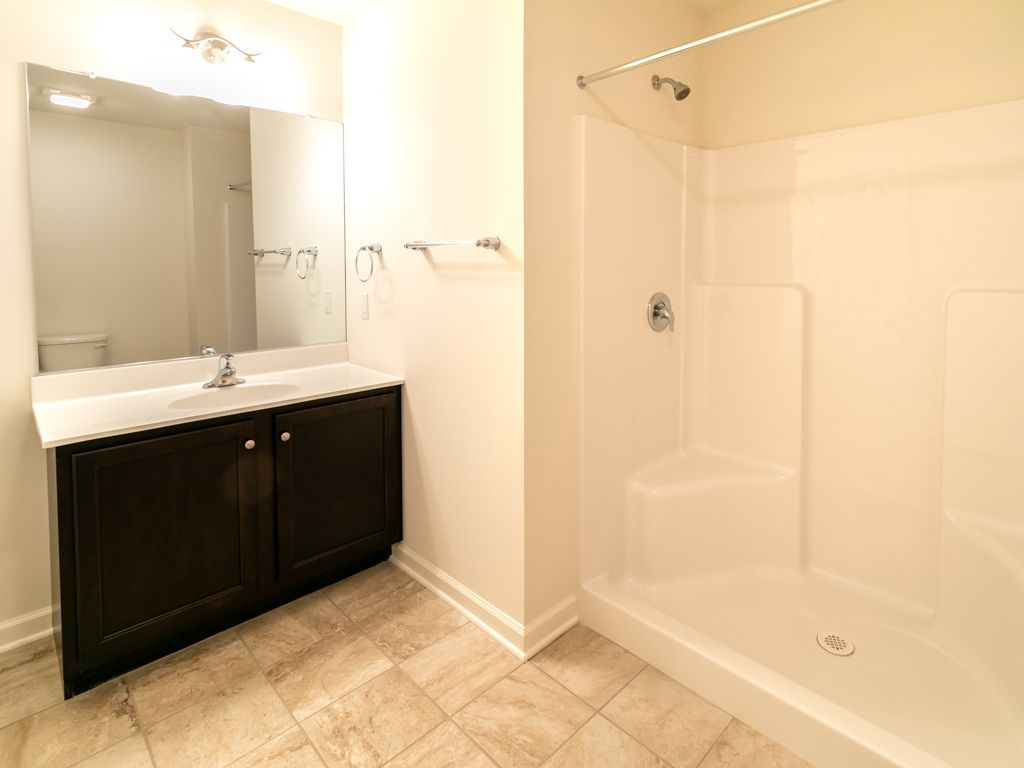 Bathroom with dark brown vanity, white shower, and beige tile floor.
