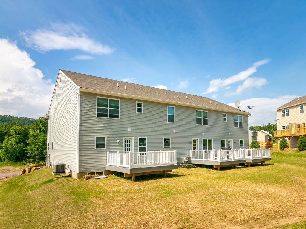 Rear view of grey townhomes with white decks on a grassy hillside under a blue sky.