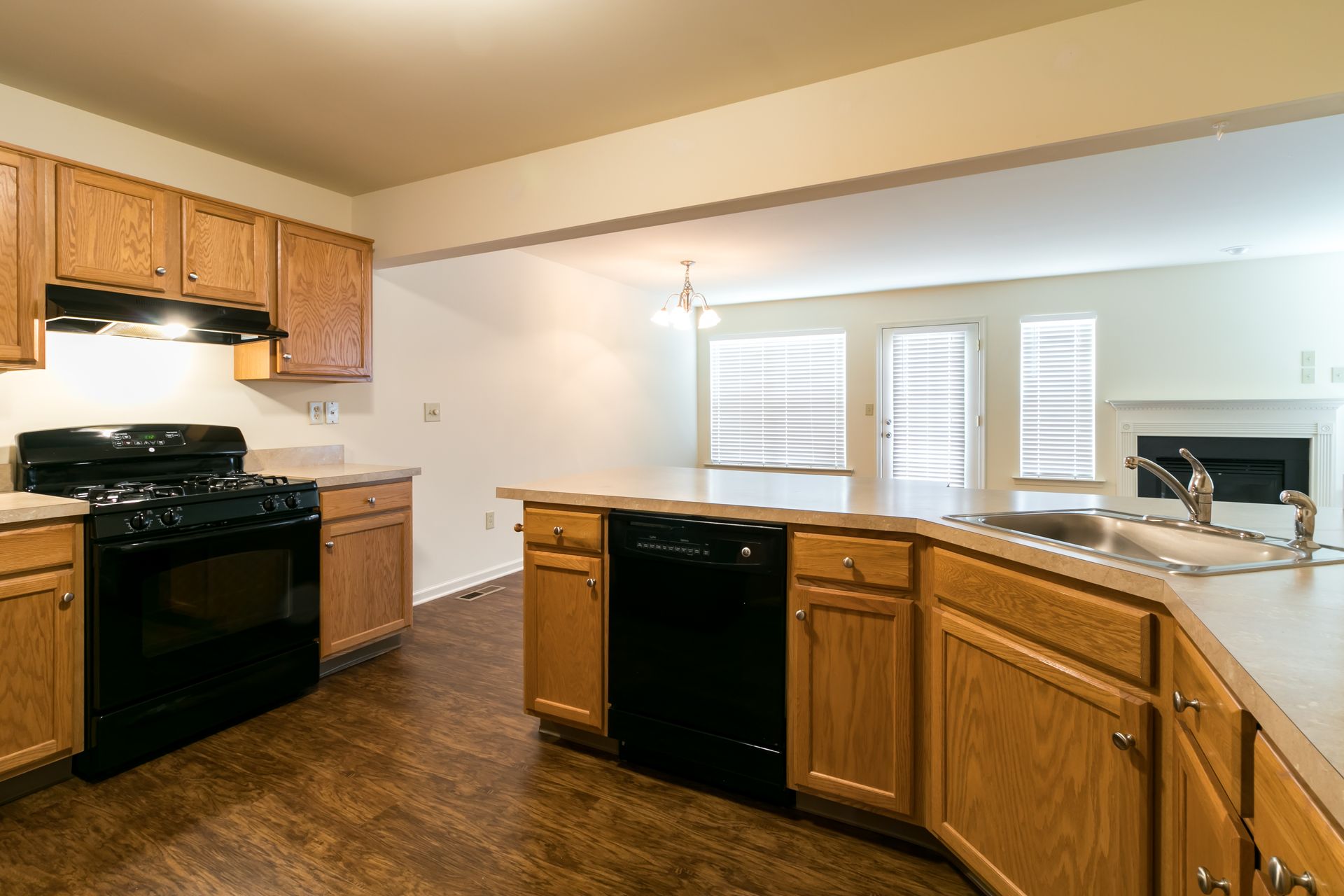 Kitchen with wood cabinets, black appliances, and view of living area with fireplace.