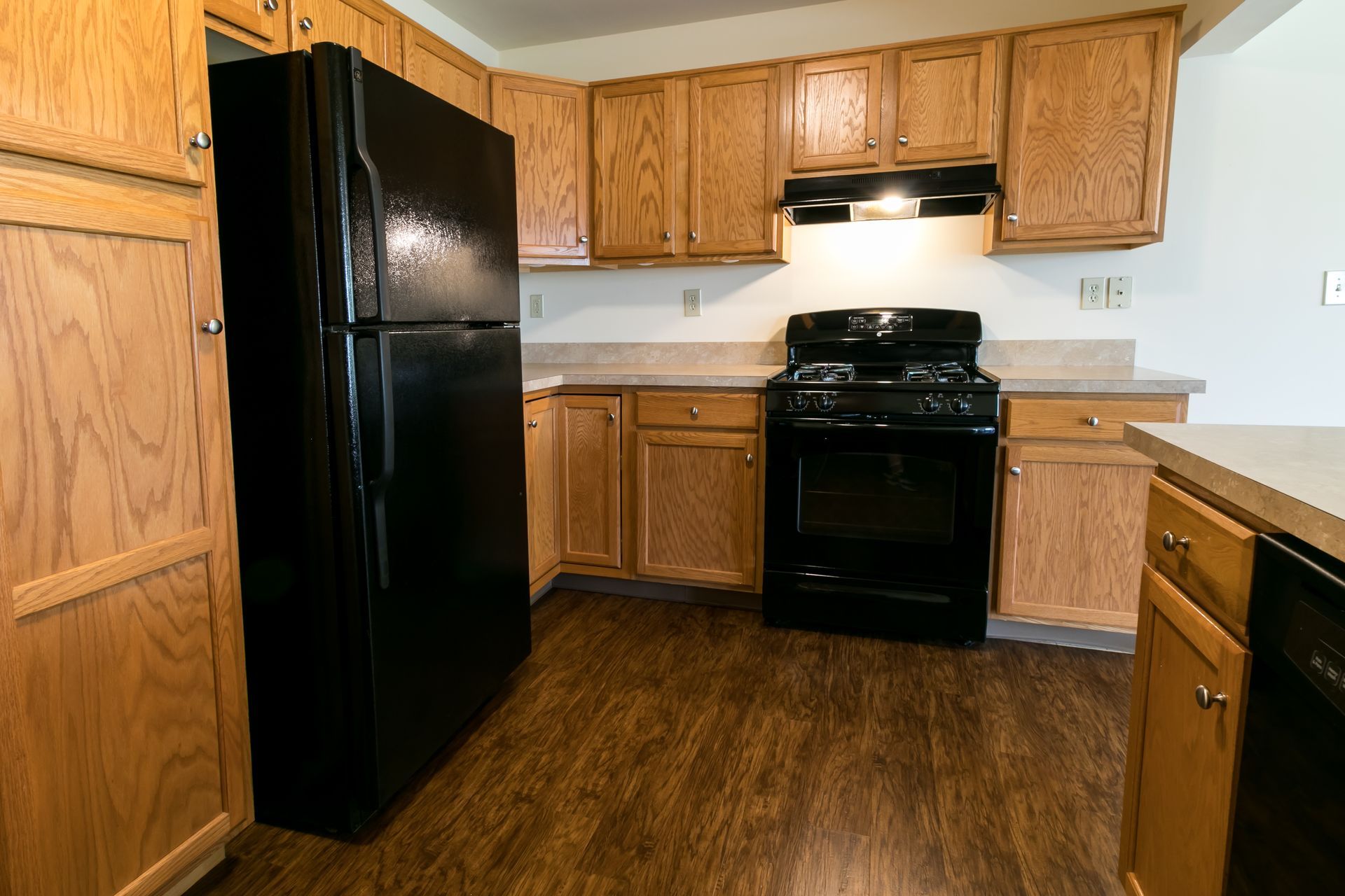 Kitchen with oak cabinets, black appliances, light countertops, and wood-look flooring.