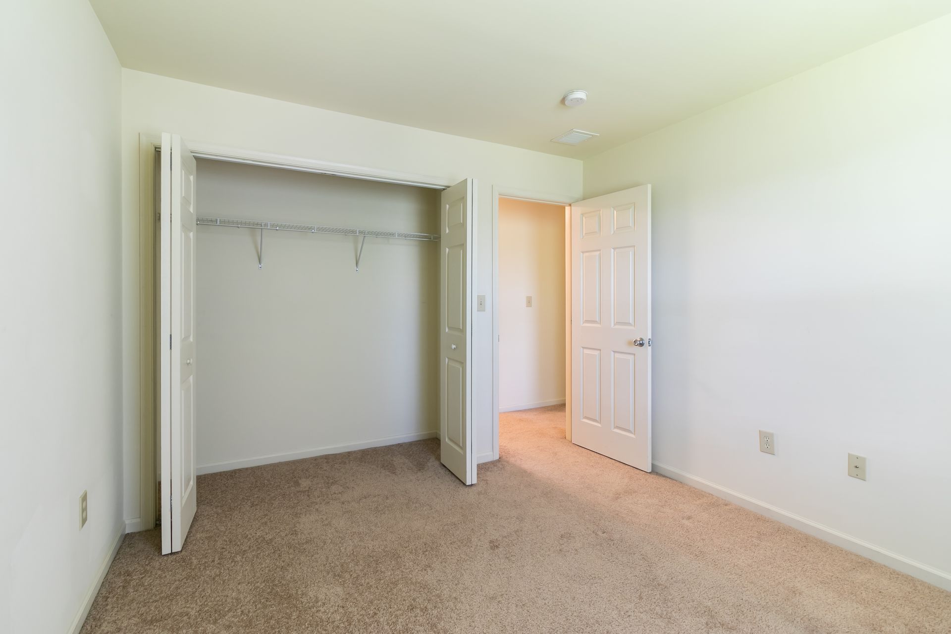 Empty bedroom with open closet and a doorway. Beige carpet and white walls.