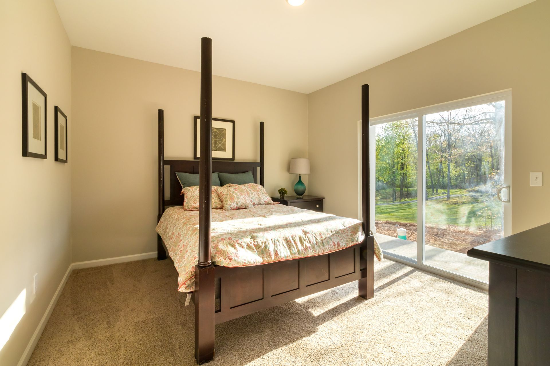 Bedroom with dark wood four-poster bed, beige walls, sliding glass door, and carpet.
