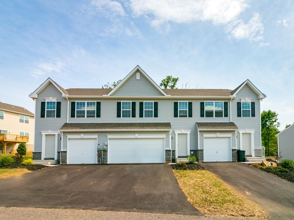 Gray townhomes with white garage doors and black shutters against a blue sky.