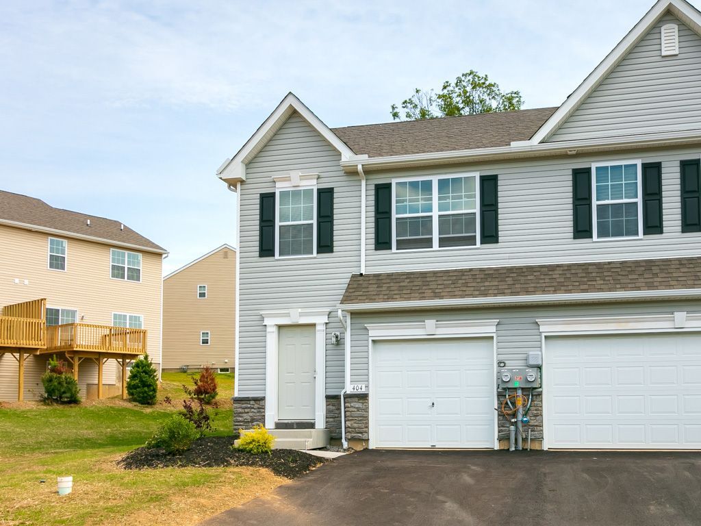 Two-story gray townhouse with white garage doors; blue sky.