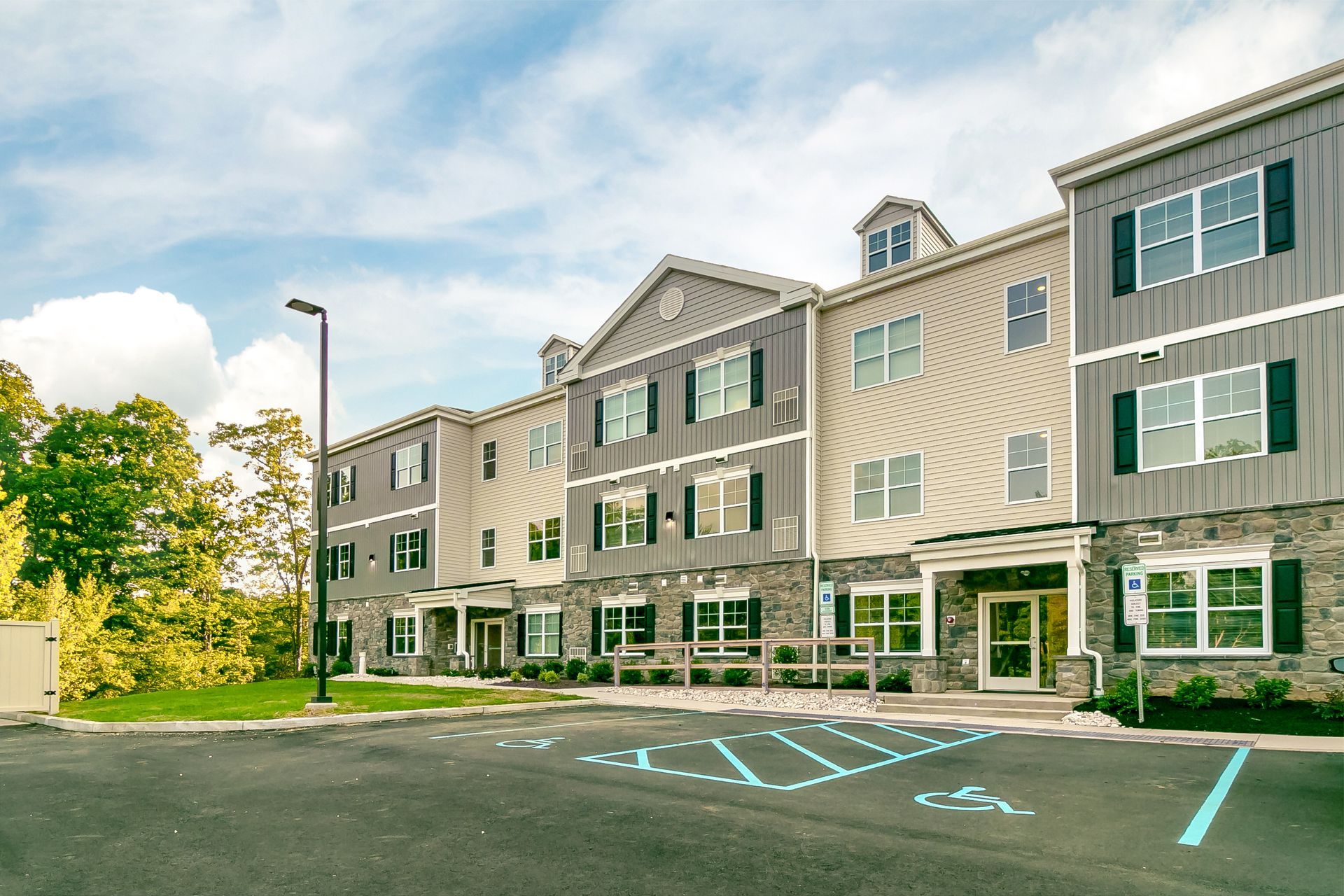 Multi-story apartment building with dark siding, stone facade, and accessible parking spaces.