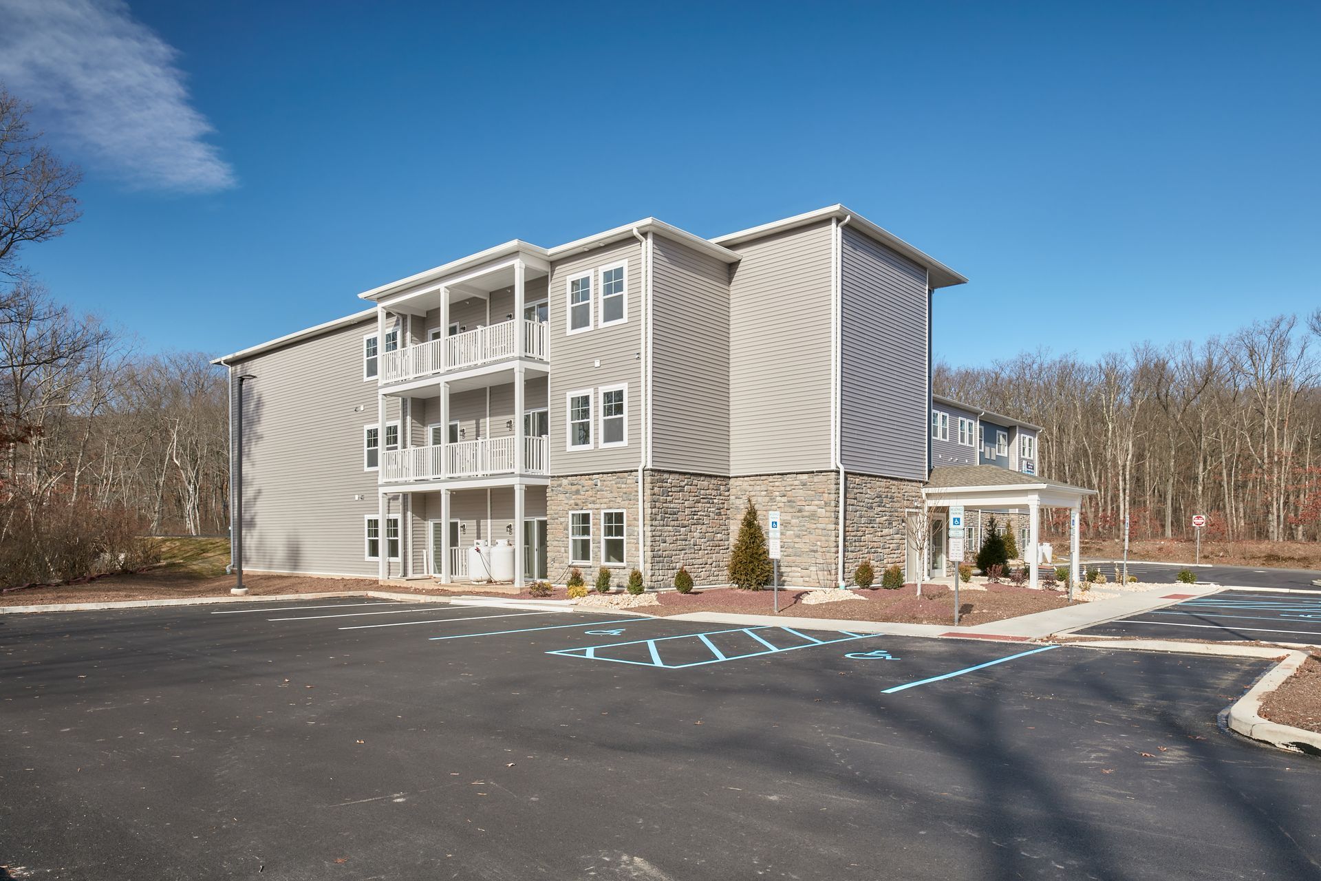 Multi-story apartment building with balconies, gray siding, stone accents, and paved parking lot.