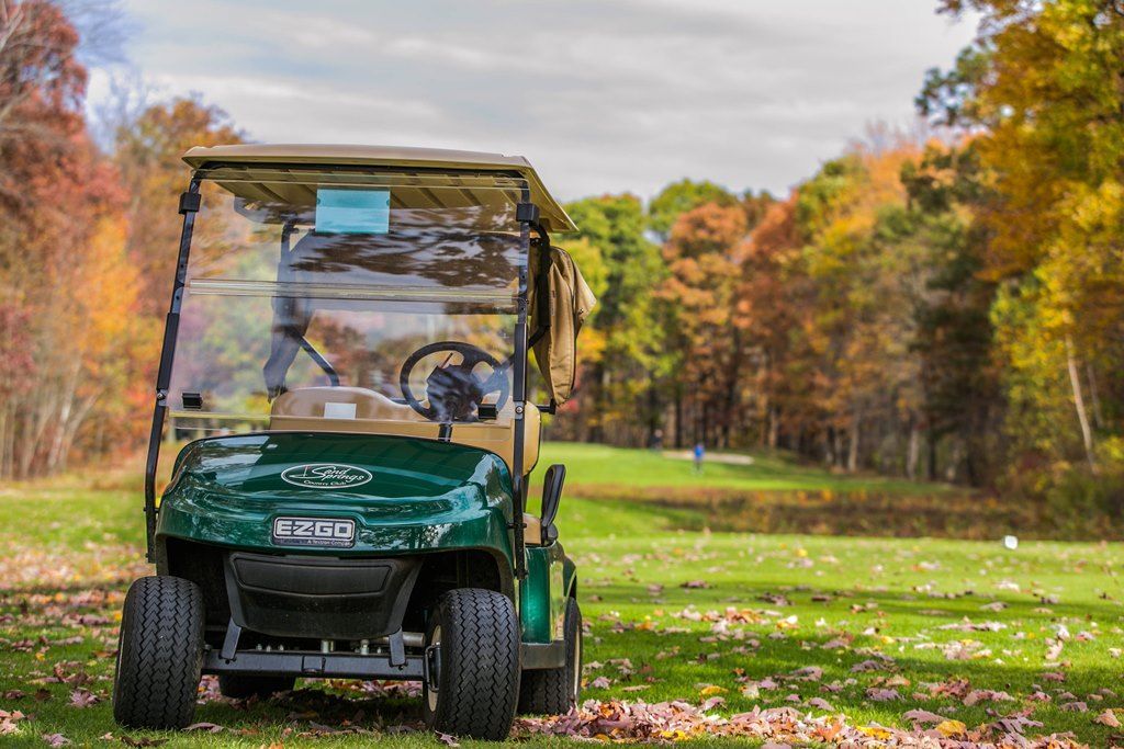 Green golf cart on a grassy course with colorful fall trees in the background.