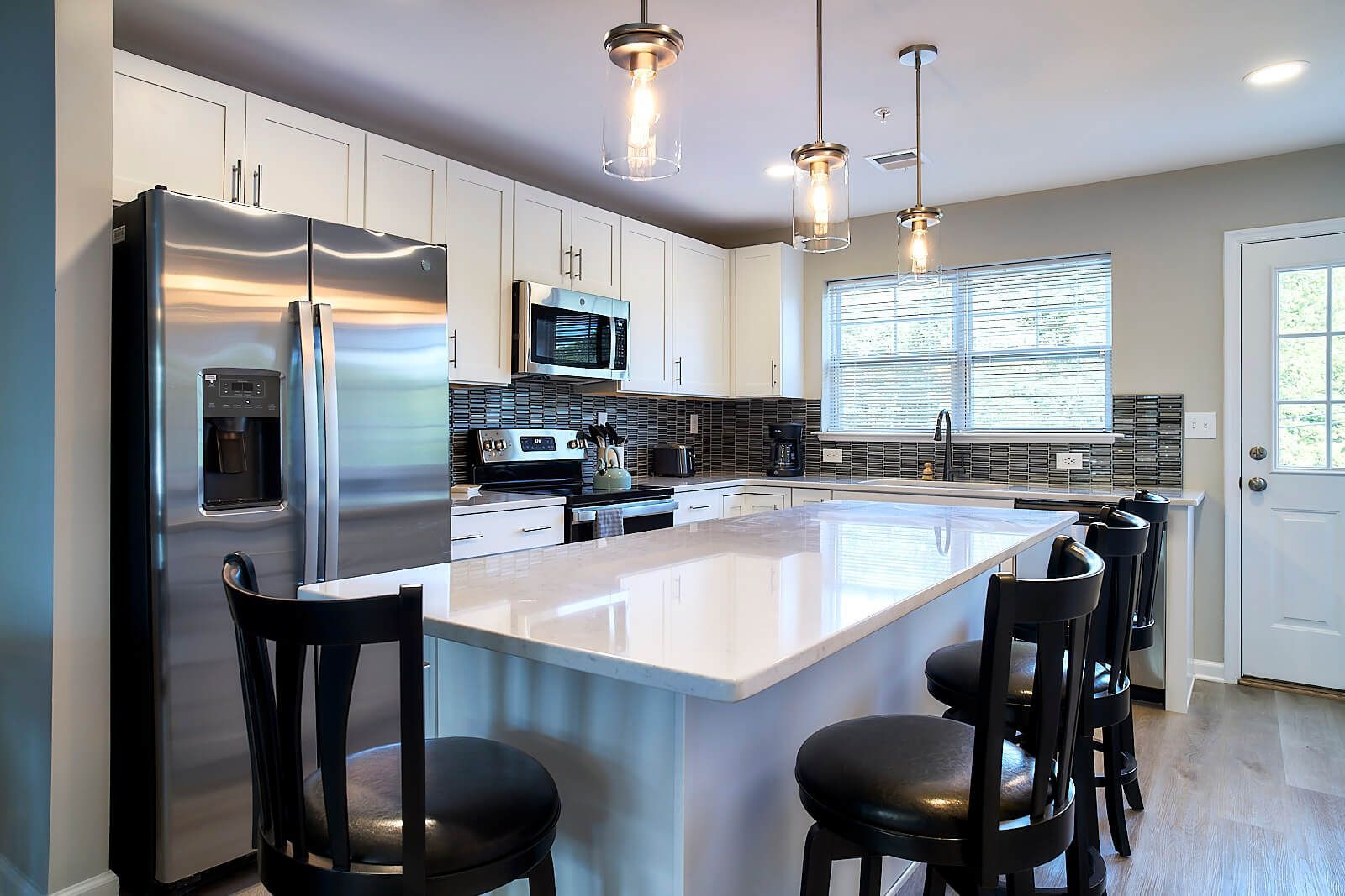 Modern kitchen with white cabinets, stainless steel appliances, island with stools.