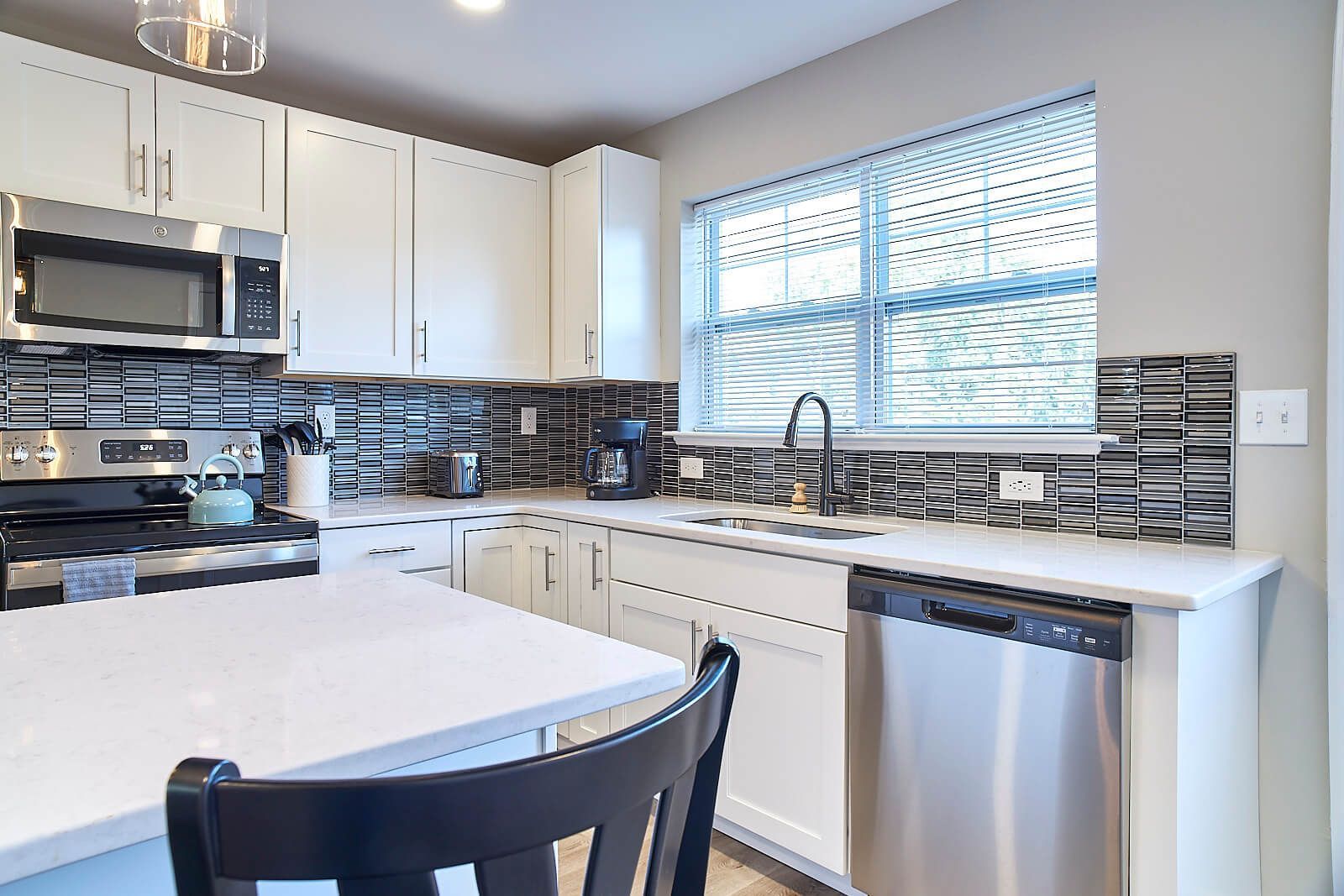 White kitchen with stainless steel appliances, black and silver backsplash, and a window.