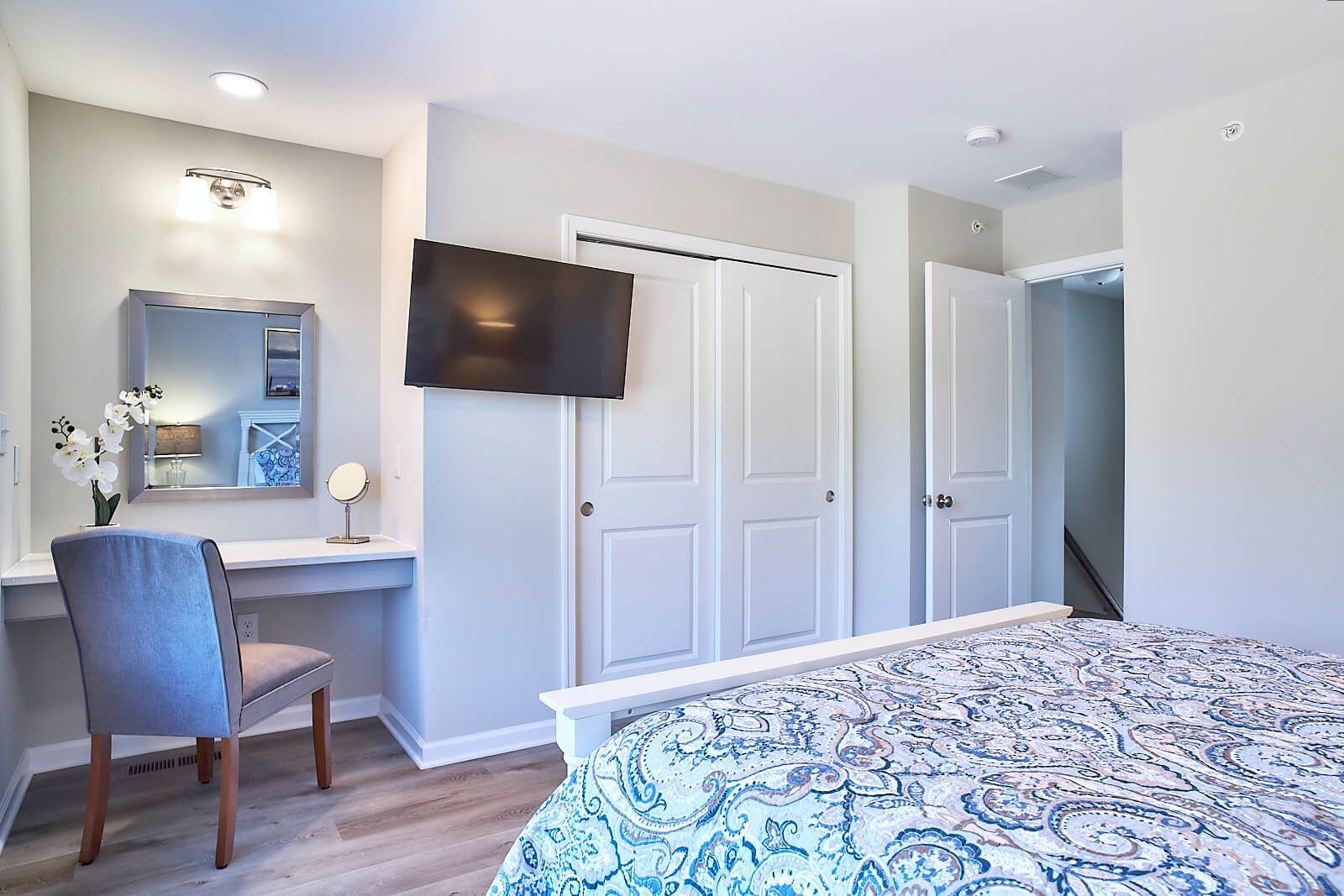 Bedroom with vanity, TV, closet, and bed; gray walls, white trim, light wood floors.