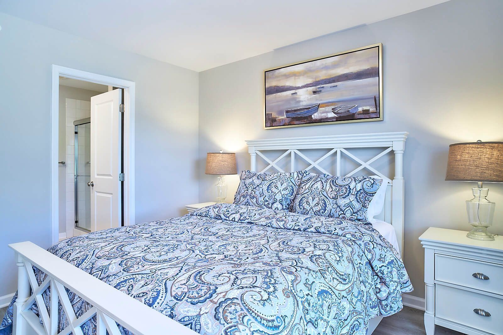 Bedroom with white bed frame, blue patterned bedding, artwork, and nightstands.