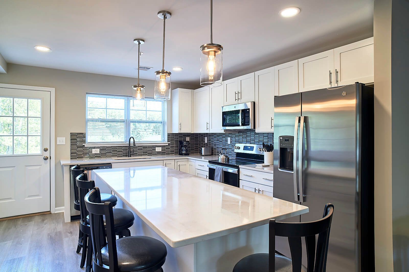Modern kitchen with white cabinets, island, stainless steel appliances, and black bar stools.