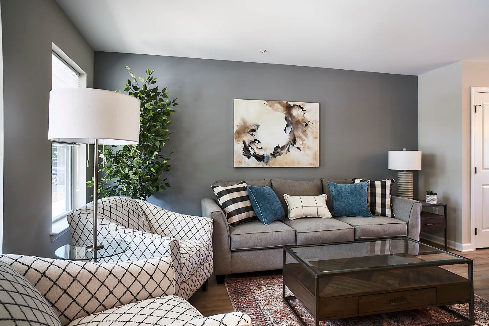 Living room with gray sofa, patterned armchair, abstract art, and a floor lamp.