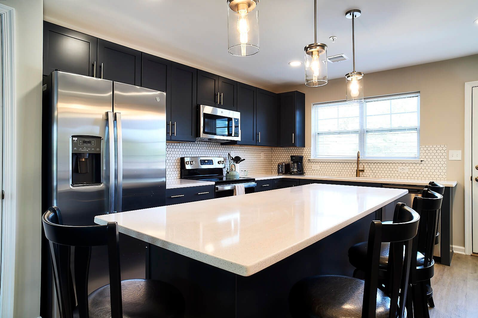 Modern kitchen with dark blue cabinets, stainless steel appliances, white island, and black chairs.