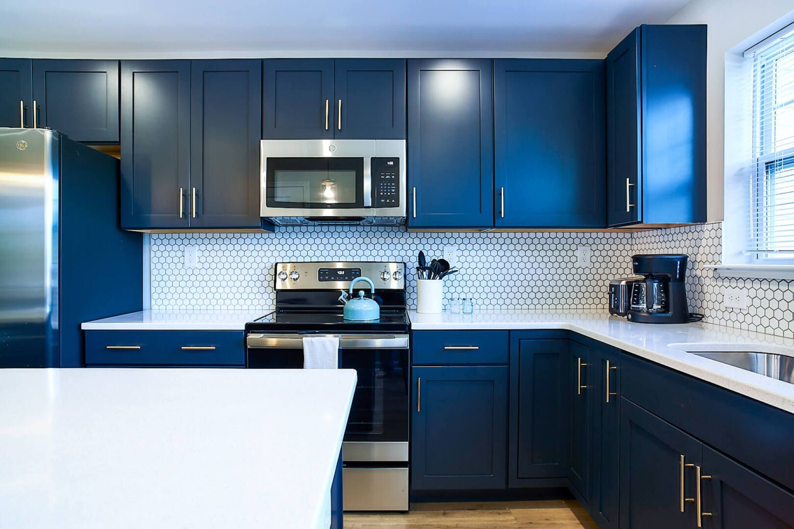 Modern kitchen with navy blue cabinets, stainless steel appliances, and white countertops.