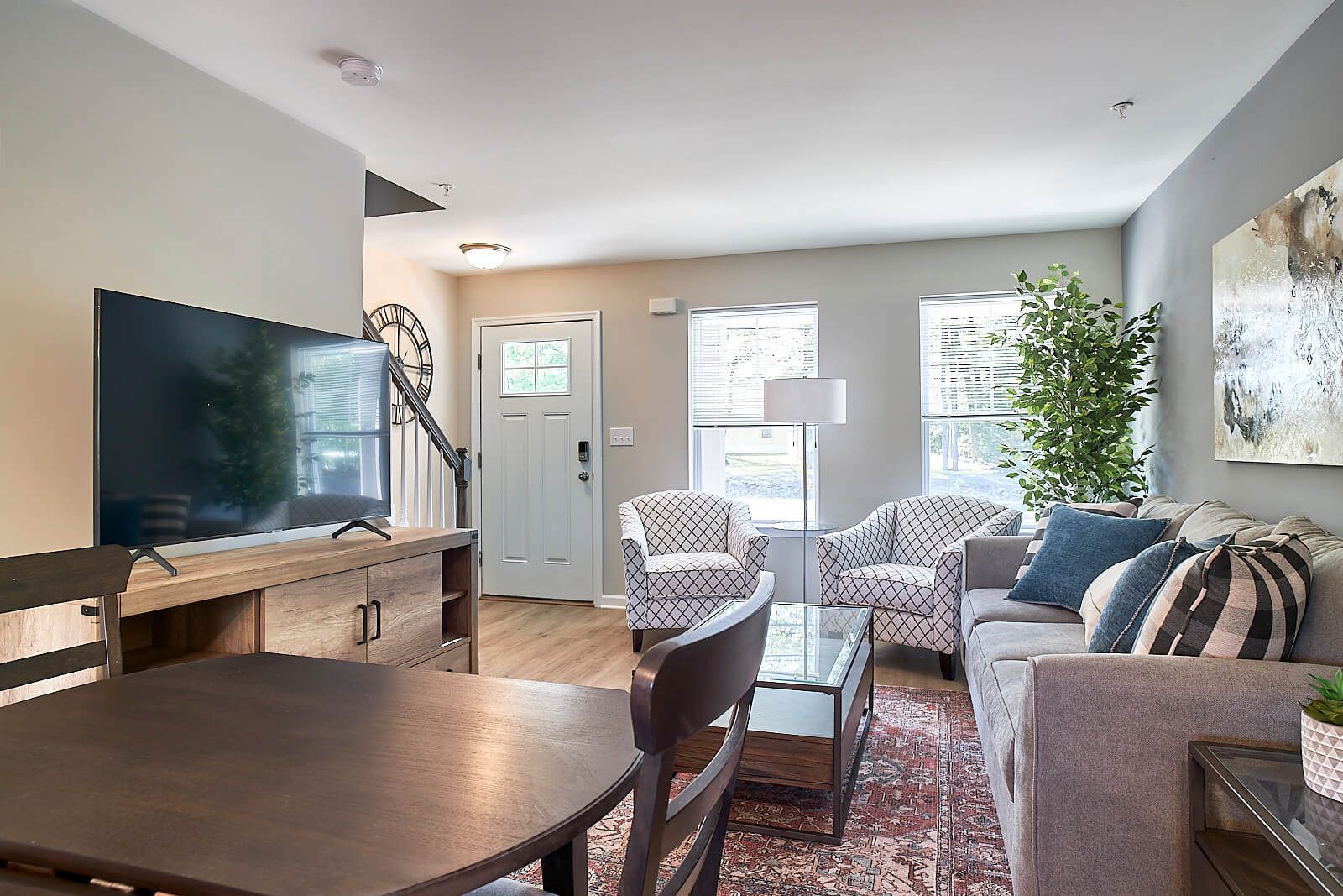 Living room with gray walls, TV, couch, patterned armchairs, dining table, and rug.