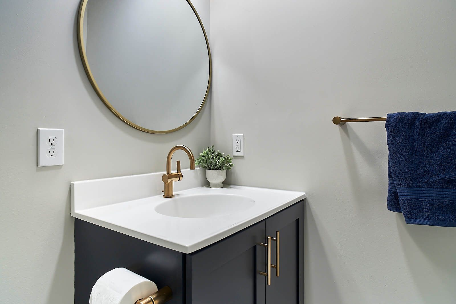 A small, modern bathroom with a navy vanity, gold fixtures, and a round mirror.