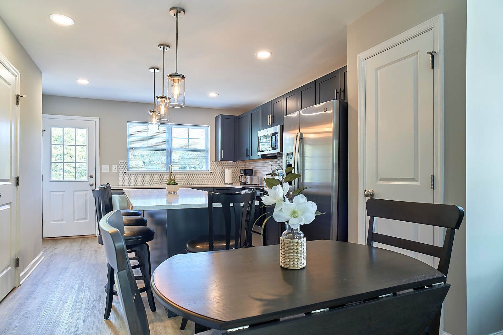 Kitchen with dark cabinets, island, and dining table; lit by pendant lights.