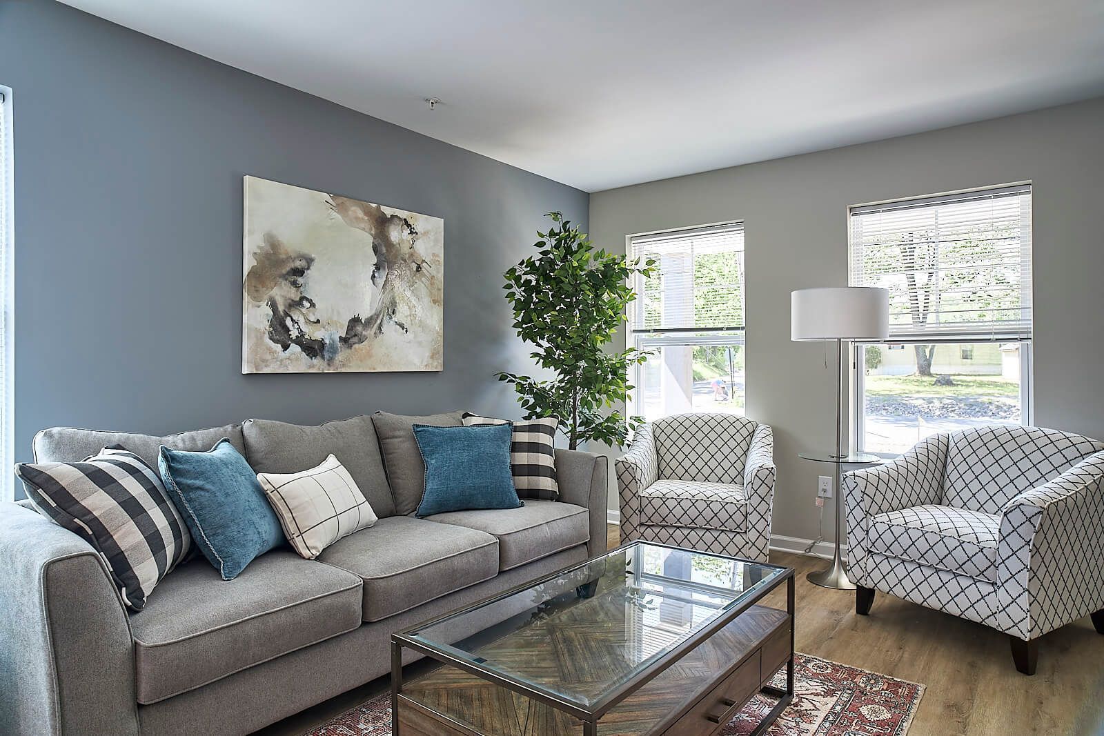 Living room with gray couch, two patterned armchairs, and abstract art on a blue wall.