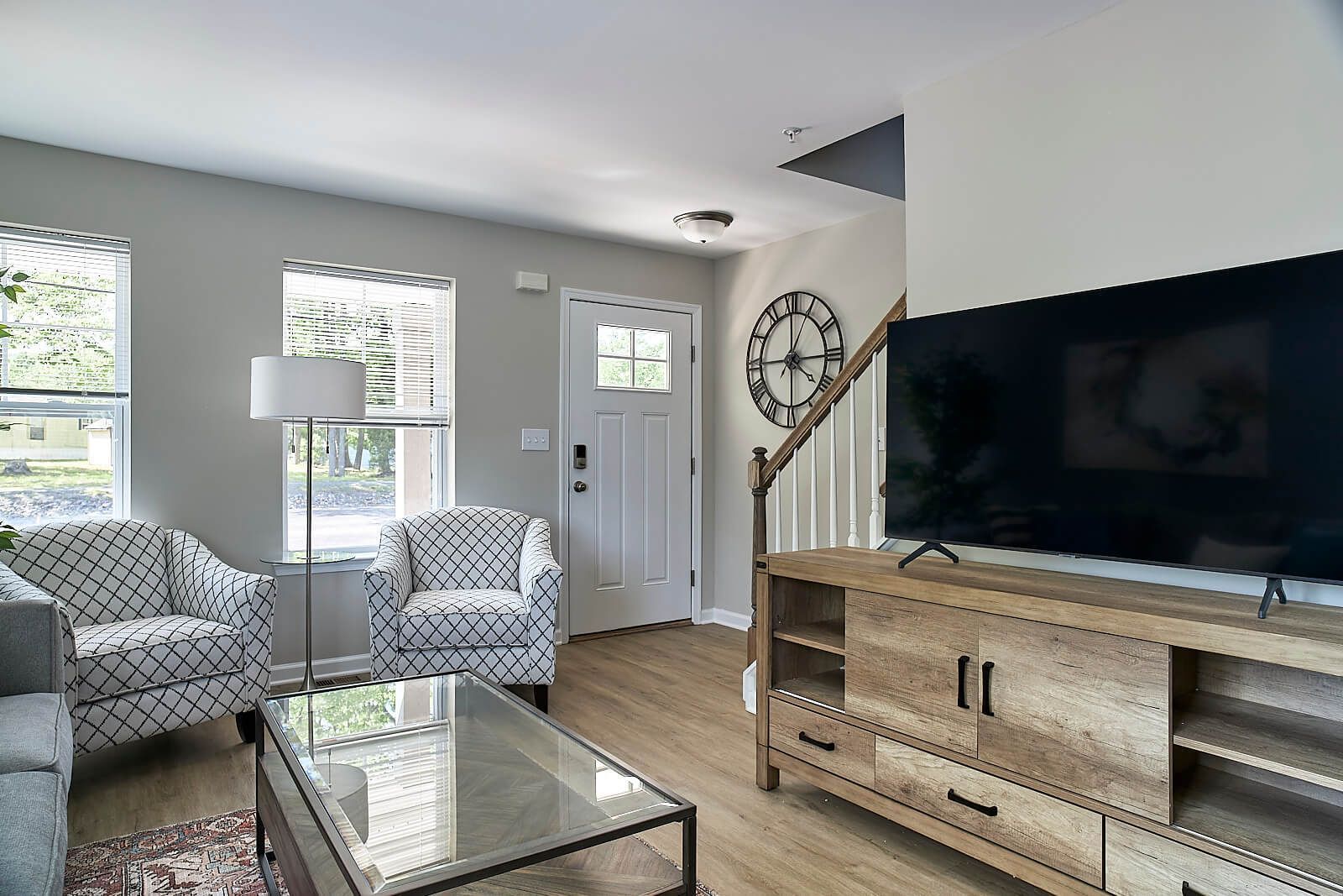 Living room with two patterned armchairs, TV, wooden console, and staircase.