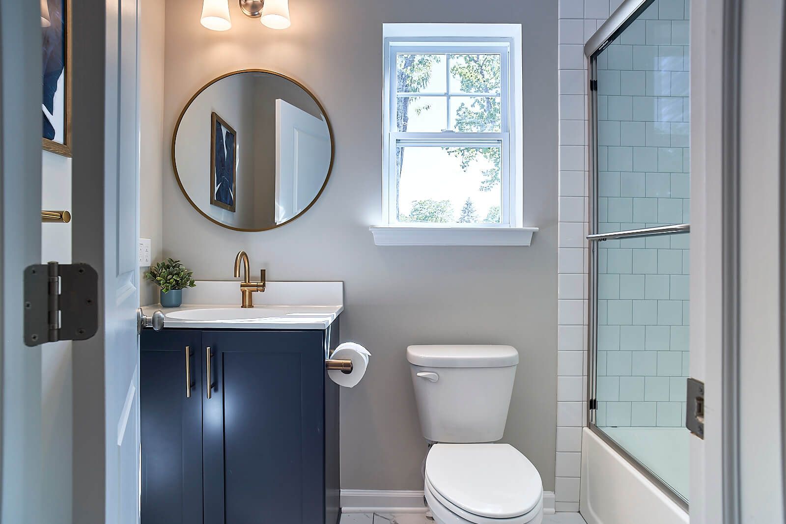 Bathroom with dark blue vanity, round mirror, white toilet, and glass shower door.