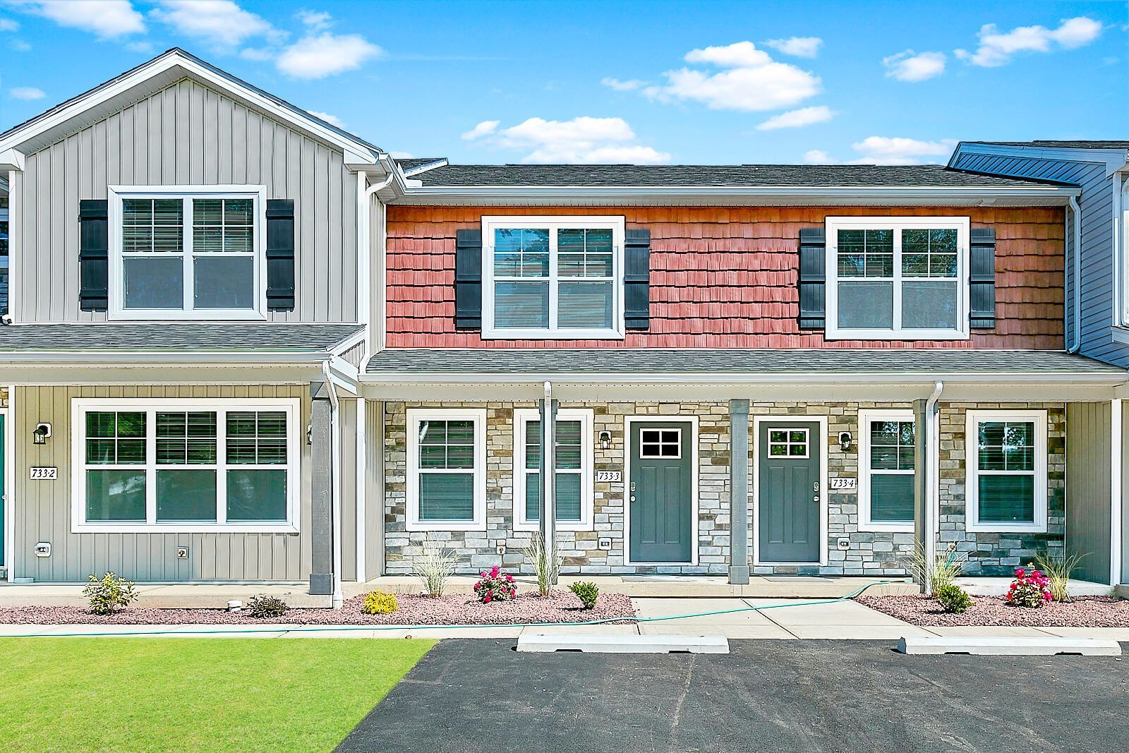 Row of townhouses with gray, red, and beige siding, white trim, and black shutters, under a blue sky.