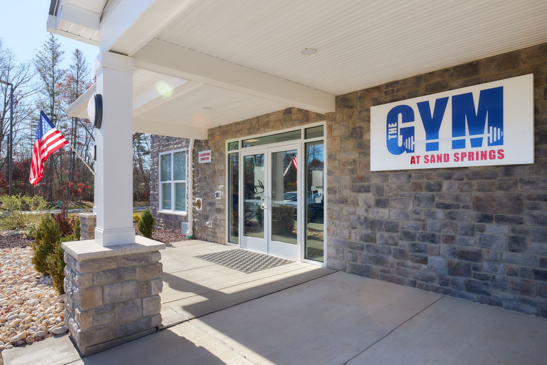 Gym entrance at Sami Springs with stone facade, glass doors, and US flag.