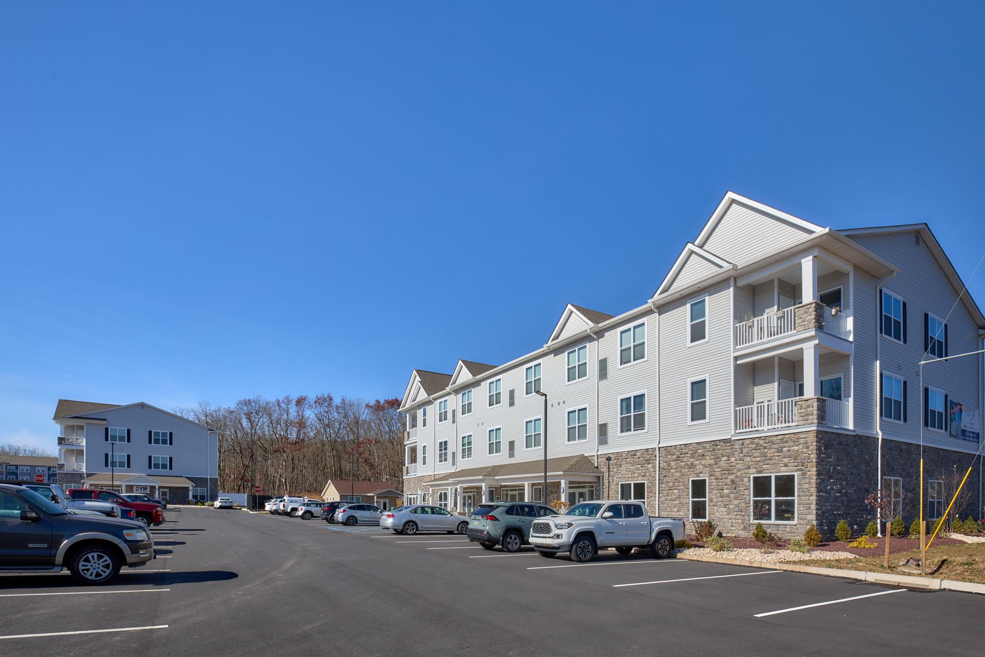 Multi-story apartment building with cars parked in front on a clear, sunny day.