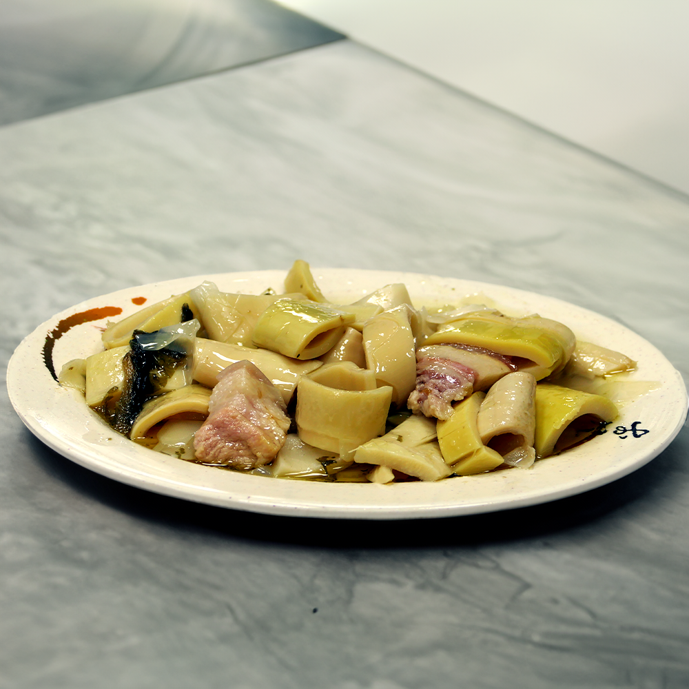 一盤食物，裡面有竹筍和豬肉。白色盤子放在灰色桌上。