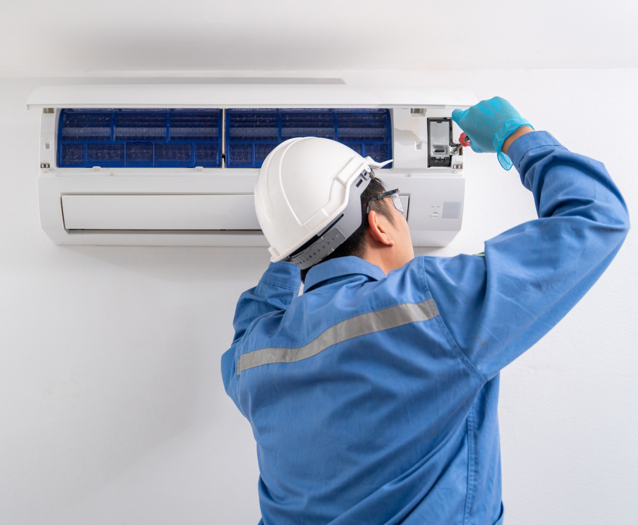 A man wearing a hard hat and gloves is working on an air conditioner.