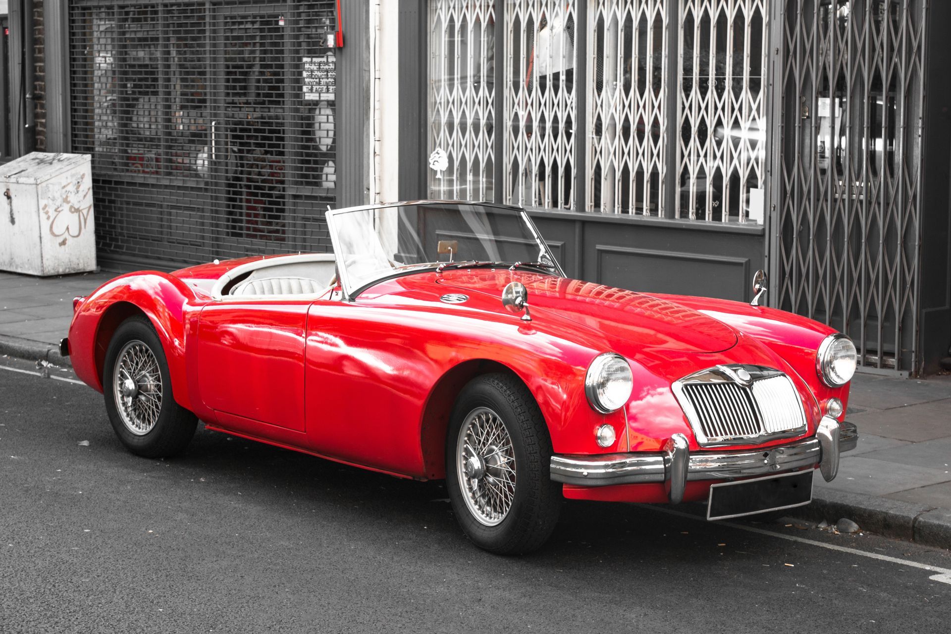 A bright red vintage convertible parked along a city street in front of metal storefront gates. A bright red vintage convertible parked along a city street in front of metal storefront gates.