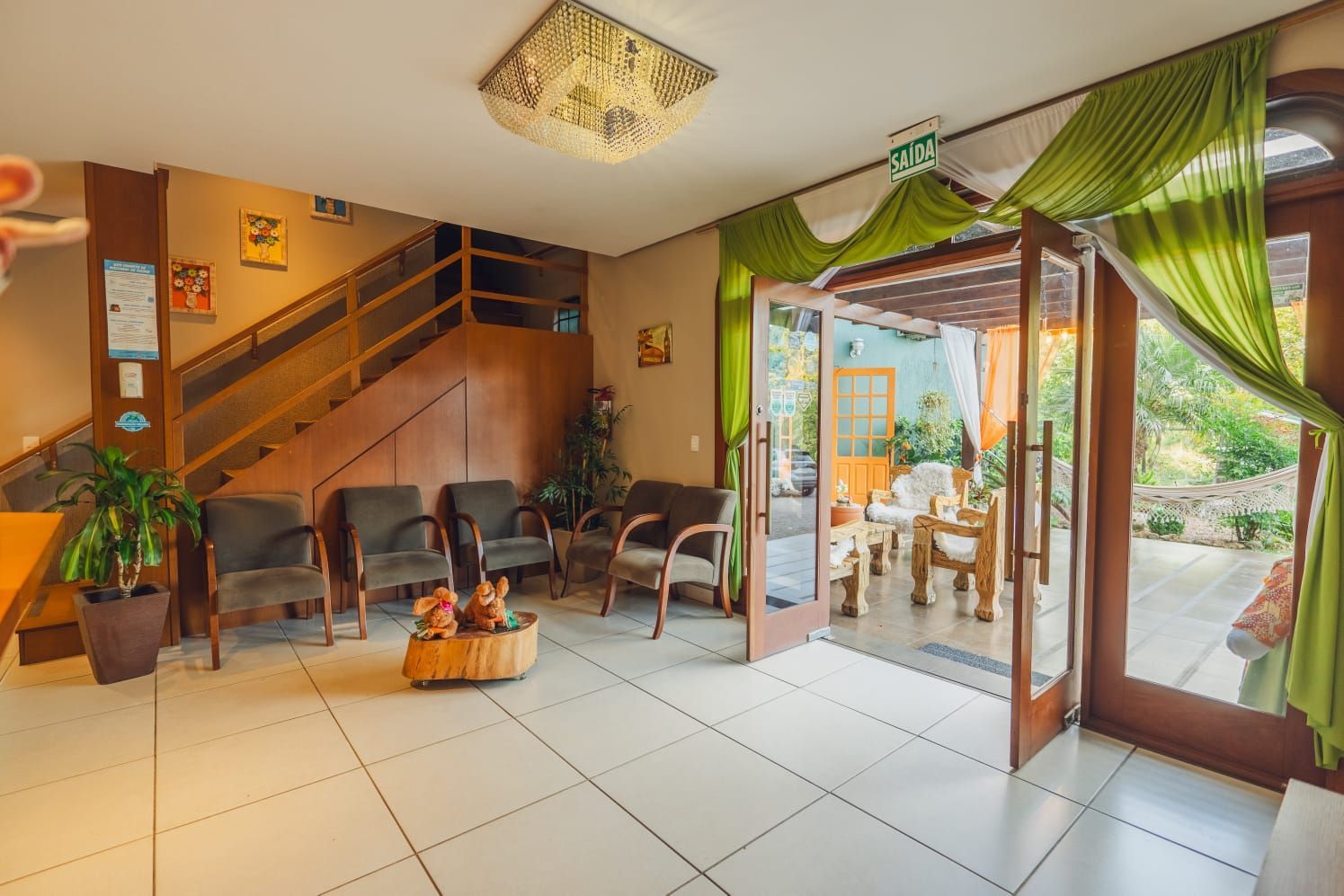 Saguão do hotel com assentos, portas abertas para uma área de jantar ao ar livre e escadas para o andar superior.