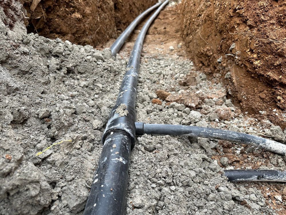 A bunch of pipes are laying in the dirt in a trench.