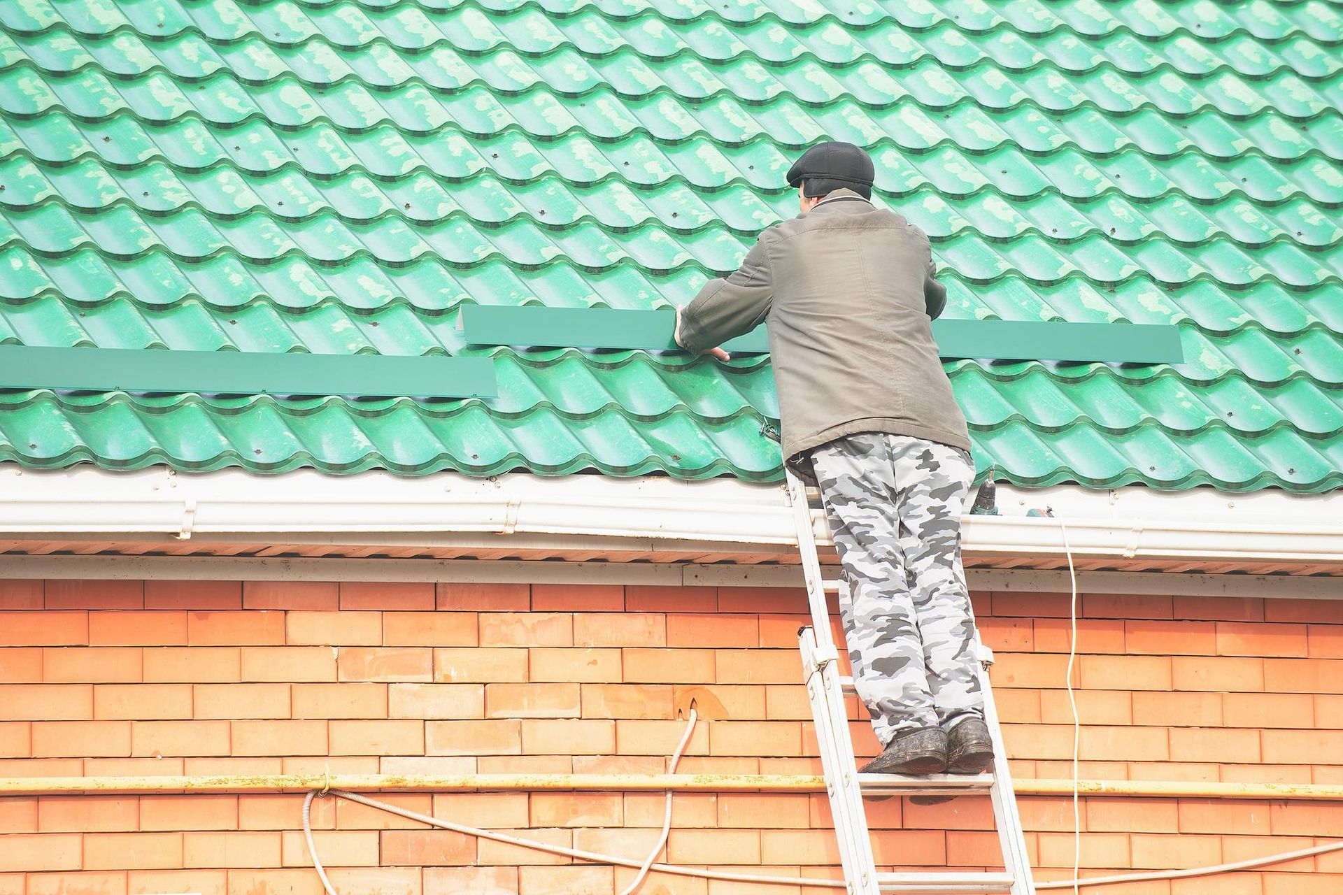 A man is standing on a ladder working on a green roof.
