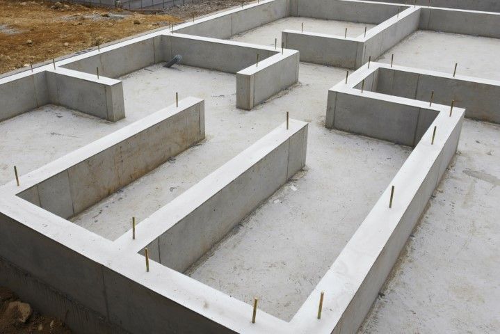 Newly poured concrete foundation walls for a building with metal anchor bolts visible on top.