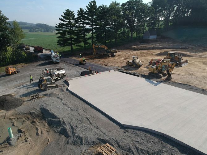An aerial view of a construction site with heavy machinery, earthwork, and a newly poured concrete pad.